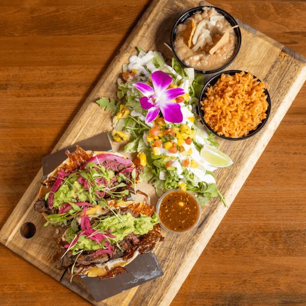 Mexican steak tacos with guacamole, pickled onions, rice, beans, and salad on a wooden board.