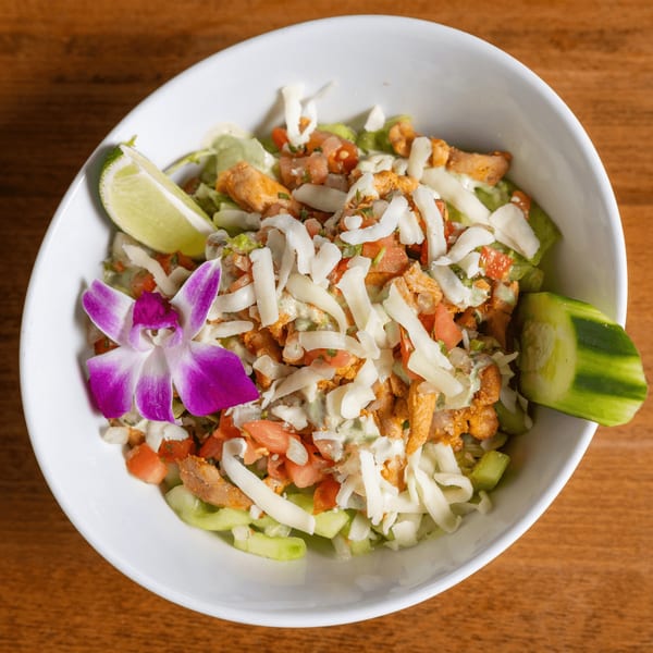 Mexican salad with chicken, shredded cheese, tomatoes, and a purple orchid in a white bowl.
