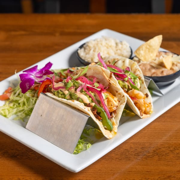Two California Tacos with rice and beans, garnished with a purple orchid on a white plate.