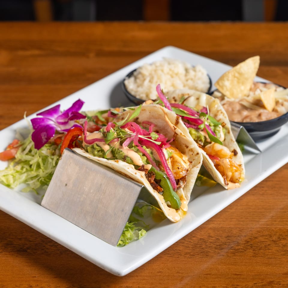 Two California Tacos with rice and beans, garnished with a purple orchid on a white plate.