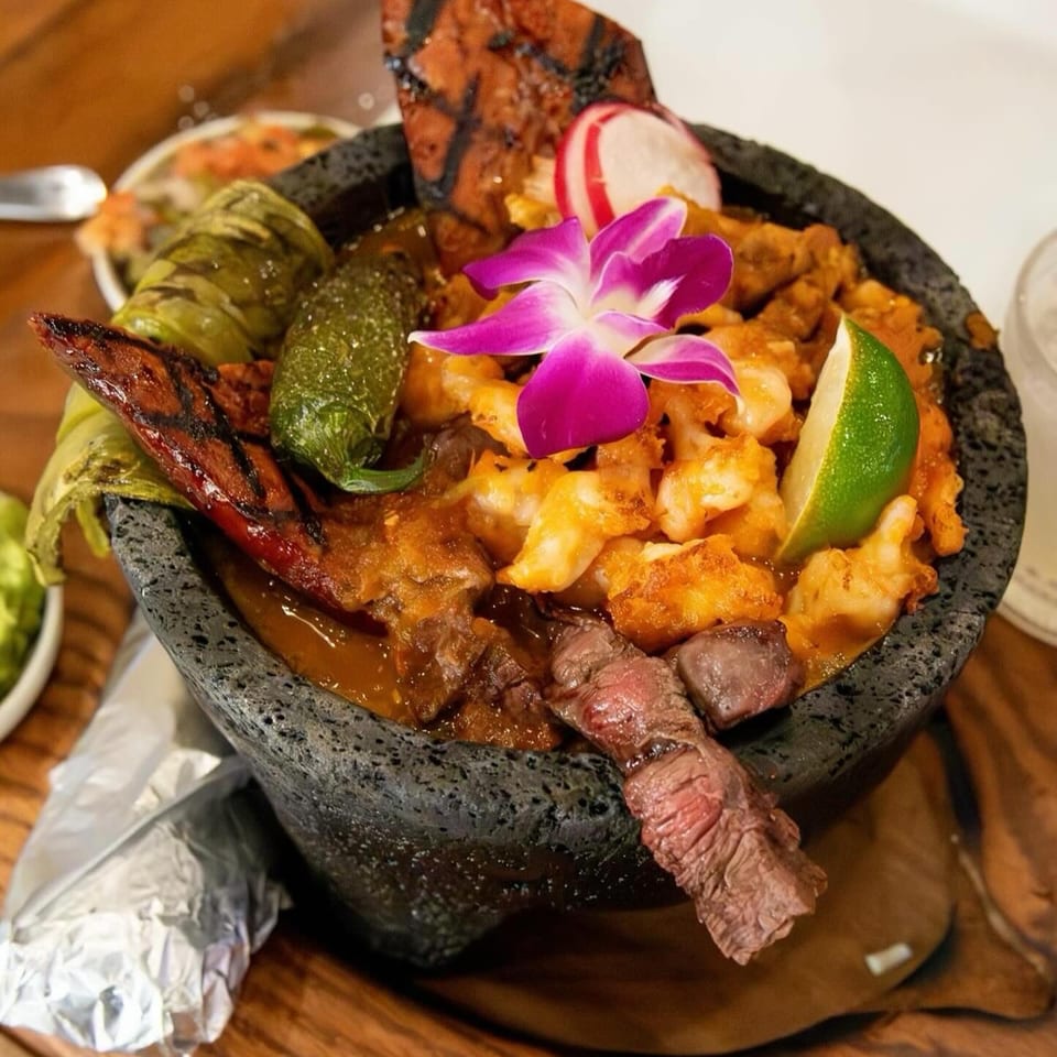 Molcajete with grilled meats, shrimp, peppers, and a purple orchid garnish at California Tacos.